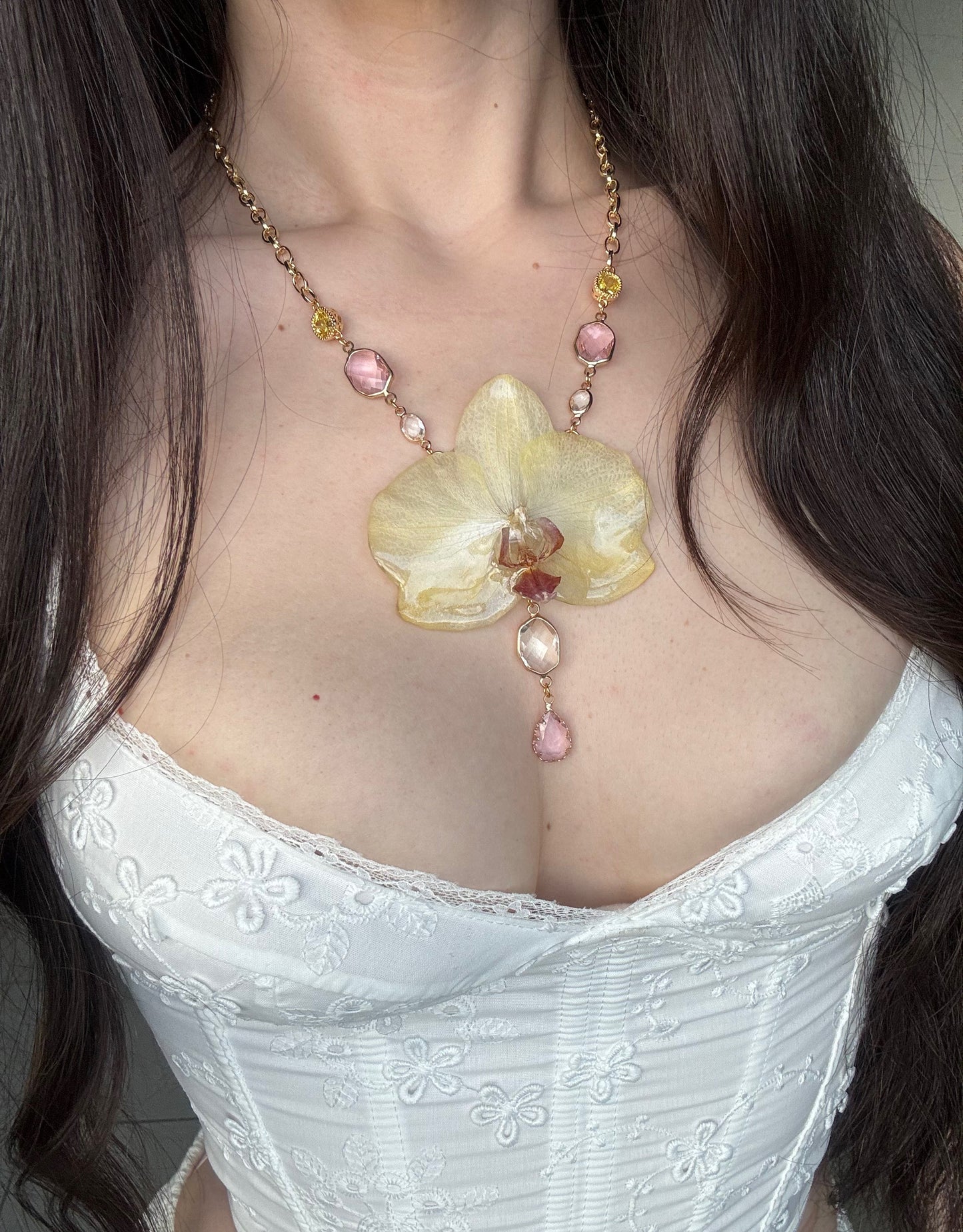 Necklace with a large yellow moth orchid pendant and pink beads on a person wearing a white lace top.